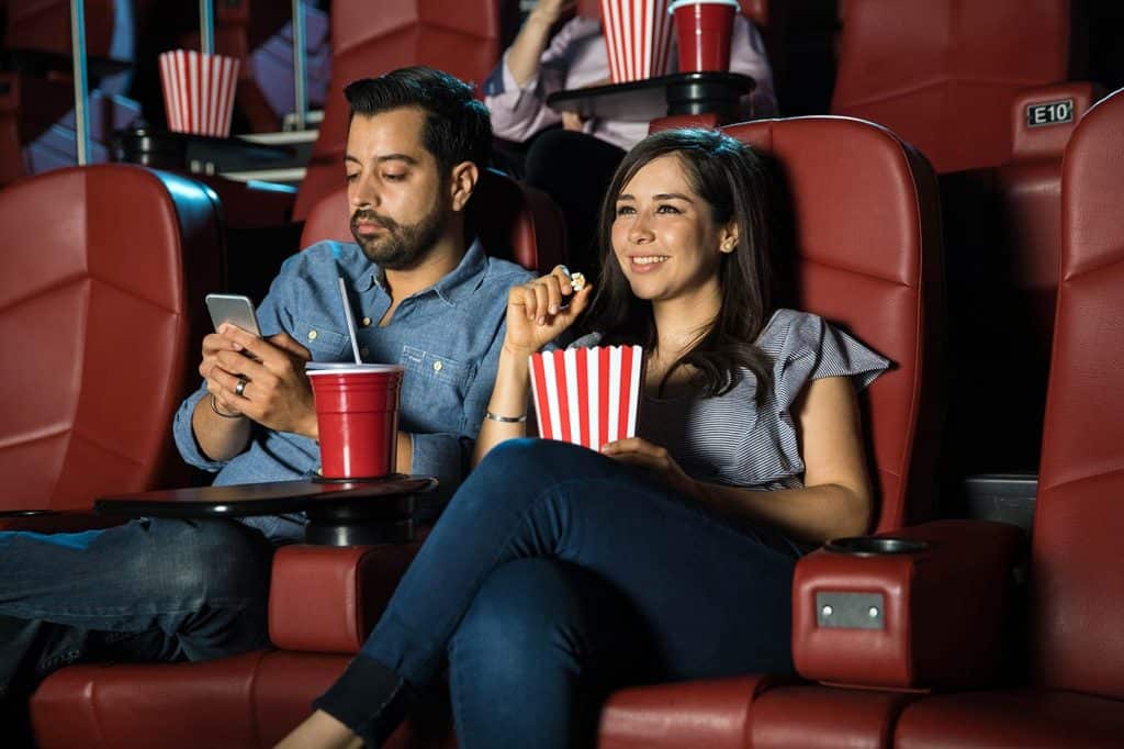 Woman enjoying movie in the cinema while her date is looking at his phone